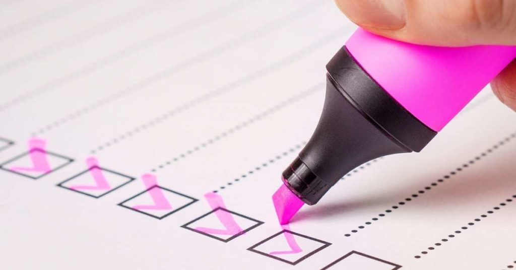 Checklist em um caderno sendo preenchido com uma caneta cor de rosa. Técnica de como ser mais produtivo e mapear as atividades